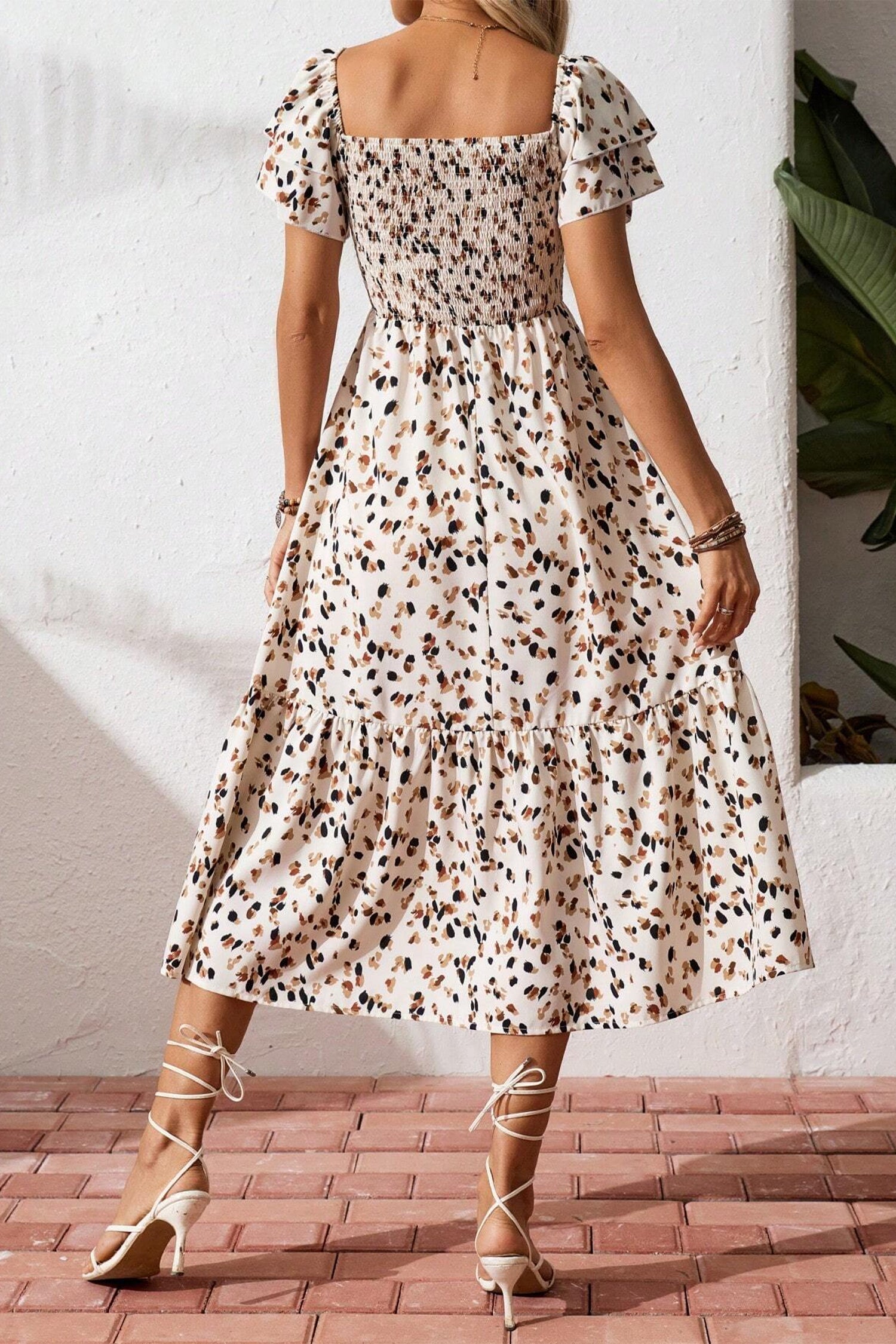 Vestido corto beige con estampado floral discreto, cuello cuadrado fruncido y mangas cortas con volantes.